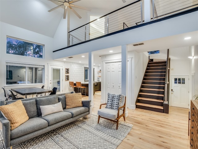 living room with ceiling fan, a towering ceiling, and light hardwood / wood-style floors