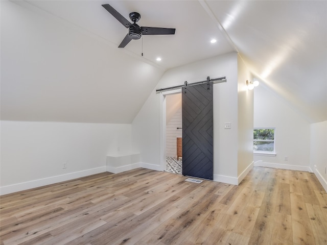 additional living space with a barn door, lofted ceiling, ceiling fan, and light hardwood / wood-style flooring