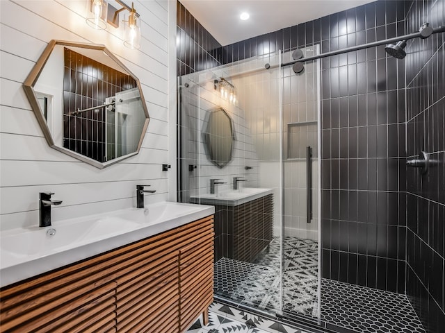 bathroom with a shower with door, dual bowl vanity, and tile walls