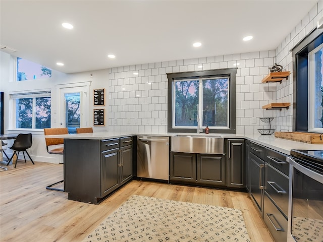 kitchen featuring kitchen peninsula, light hardwood / wood-style flooring, appliances with stainless steel finishes, tile walls, and sink