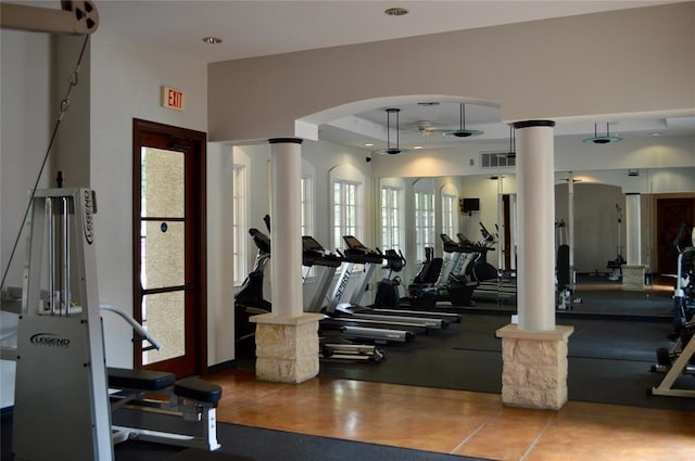 exercise room featuring a wealth of natural light, decorative columns, and a tray ceiling