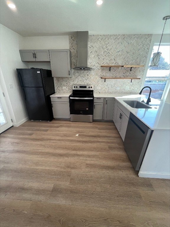 kitchen featuring stainless steel range with electric cooktop, wall chimney exhaust hood, sink, light wood-type flooring, and black fridge