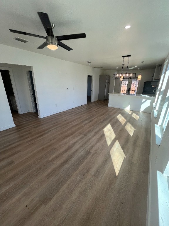 unfurnished living room with plenty of natural light, dark hardwood / wood-style flooring, and ceiling fan with notable chandelier