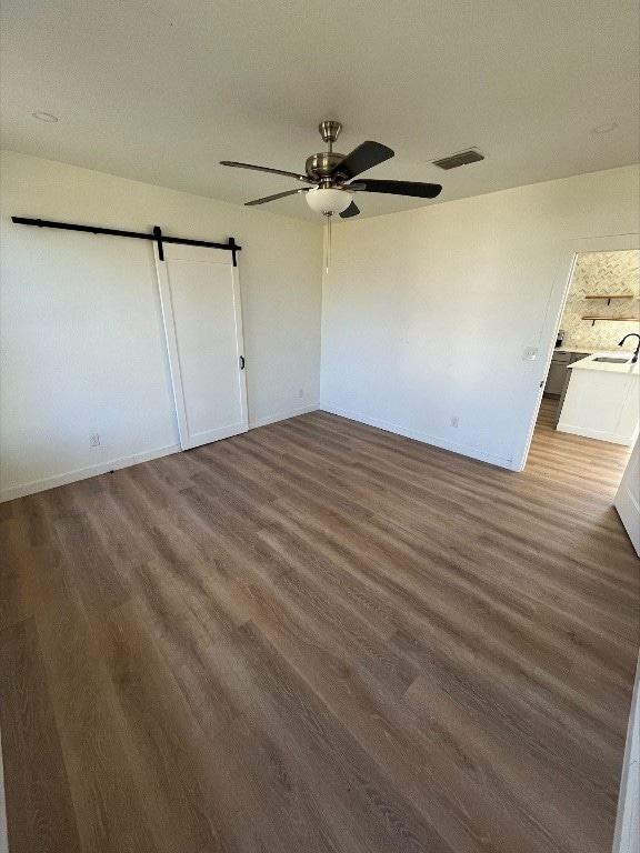 unfurnished bedroom with a barn door, ceiling fan, dark wood-type flooring, and sink