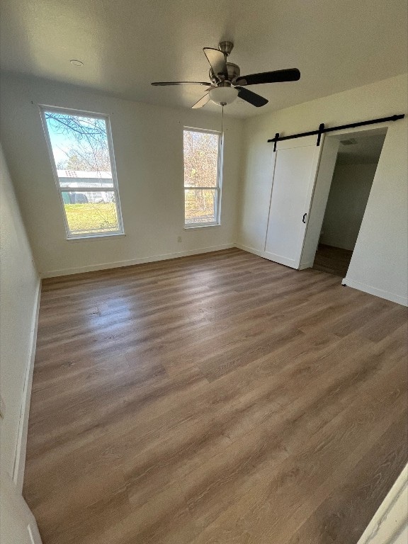 unfurnished bedroom with a barn door, a closet, ceiling fan, and hardwood / wood-style flooring