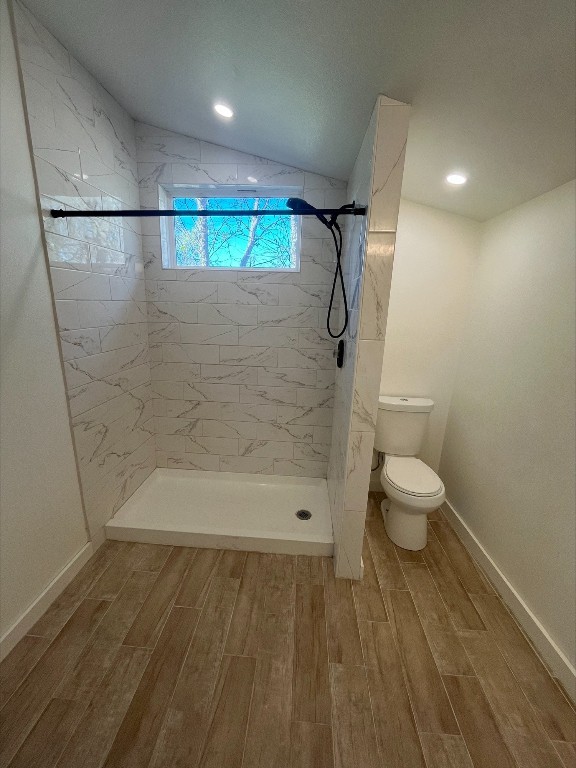 bathroom with lofted ceiling, toilet, a tile shower, and wood-type flooring