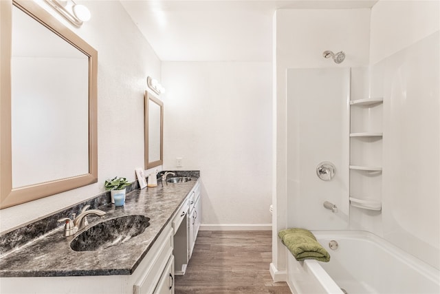 full bathroom with toilet, vanity with extensive cabinet space, wood-type flooring, dual sinks, and shower / bathtub combination