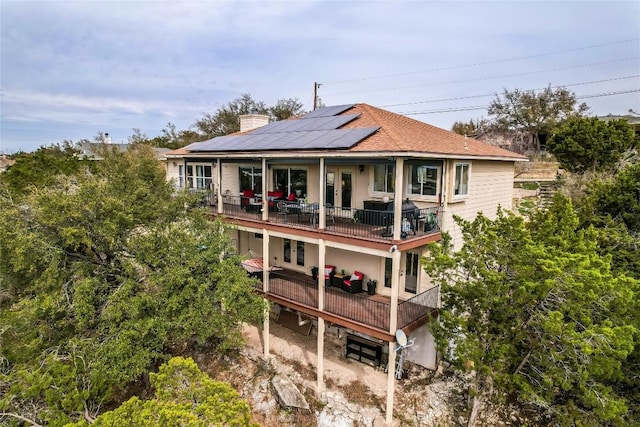 rear view of property featuring a balcony, a chimney, solar panels, and french doors