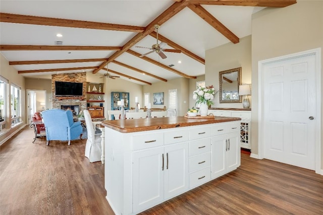 kitchen with lofted ceiling with beams, a stone fireplace, dark wood-style floors, and white cabinetry