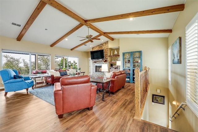 living area with vaulted ceiling with beams, ceiling fan, a fireplace, visible vents, and light wood finished floors