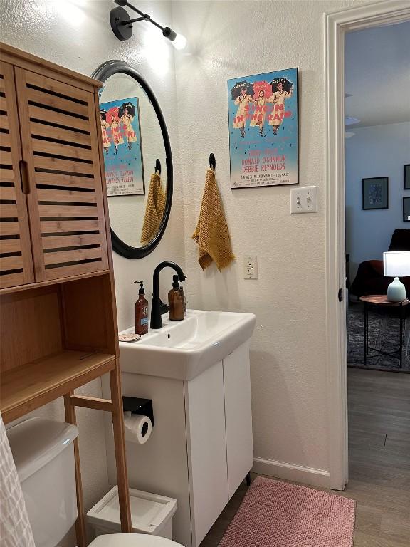 1301 NE 2nd St, Smithville, TX 78957 - bathroom with vanity, toilet, a textured wall, baseboards, and wood finished floors