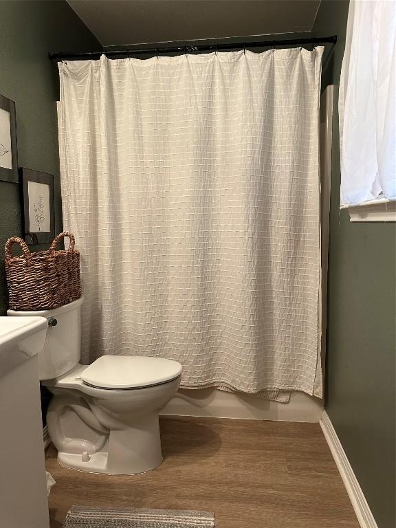 1301 NE 2nd St, Smithville, TX 78957 - bathroom featuring baseboards, wood finished floors, toilet, and shower / bathtub combination with curtain