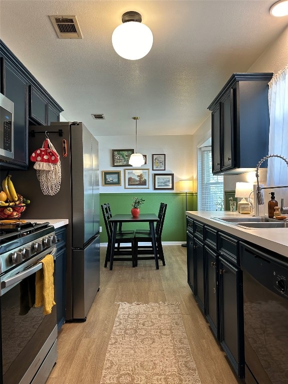 kitchen with hanging light fixtures, black dishwasher, high end stainless steel range oven, light hardwood / wood-style flooring, and sink