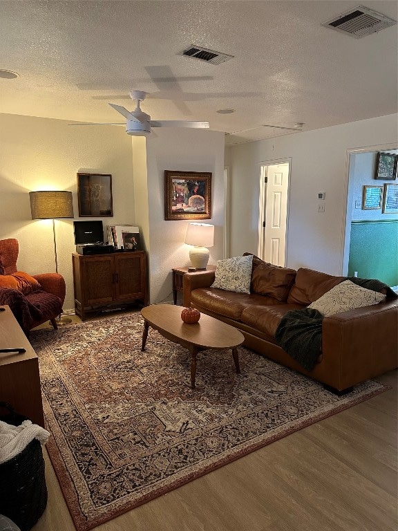 living room with ceiling fan, a textured ceiling, and wood-type flooring