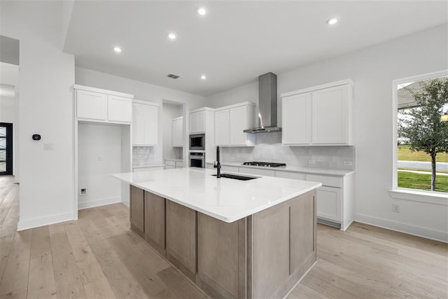 kitchen with a kitchen island with sink, sink, wall chimney exhaust hood, white cabinetry, and stainless steel appliances