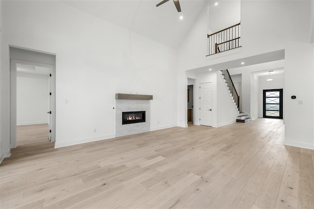 unfurnished living room with a high end fireplace, high vaulted ceiling, light hardwood / wood-style floors, and ceiling fan