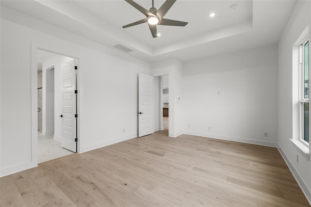 unfurnished bedroom with a tray ceiling, ceiling fan, and light wood-type flooring