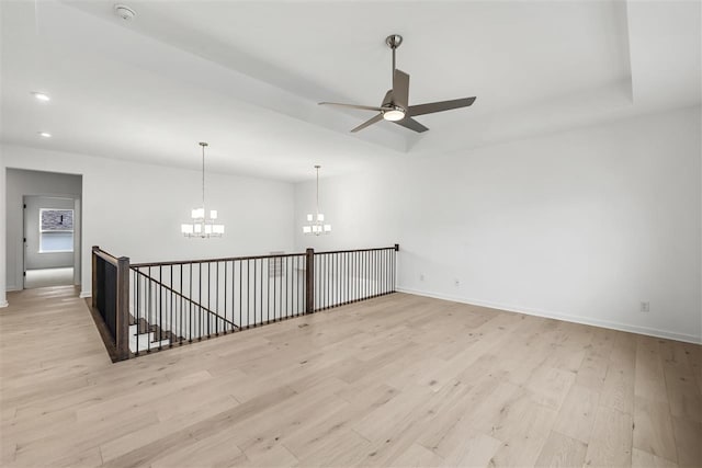 spare room with ceiling fan with notable chandelier and light wood-type flooring