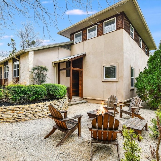 rear view of property featuring a patio area, a fire pit, and stucco siding