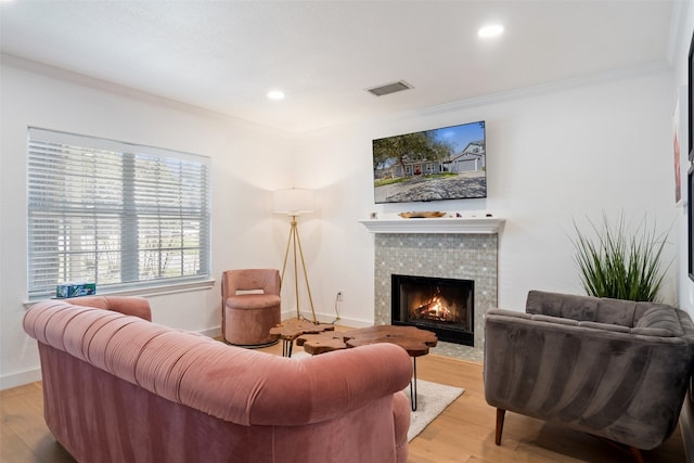 living room featuring a tile fireplace, light hardwood / wood-style flooring, and ornamental molding