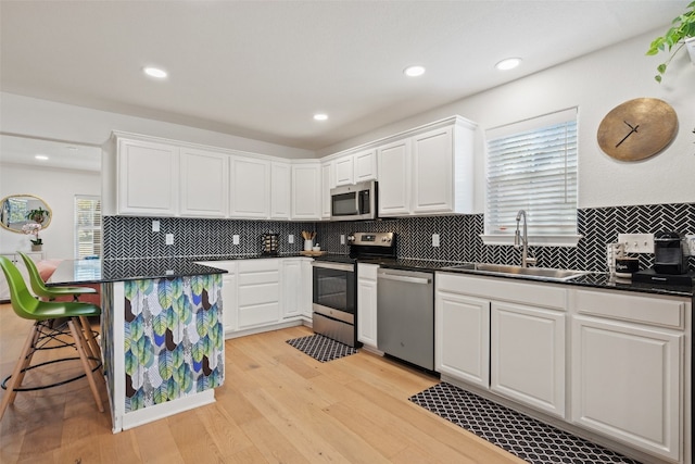 kitchen featuring white cabinetry, sink, light hardwood / wood-style floors, a breakfast bar, and appliances with stainless steel finishes