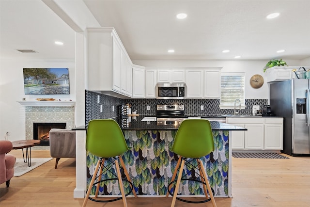 kitchen with sink, stainless steel appliances, light hardwood / wood-style floors, a breakfast bar, and white cabinets