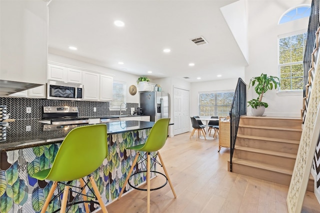 kitchen featuring appliances with stainless steel finishes, white cabinetry, a breakfast bar area, and a healthy amount of sunlight