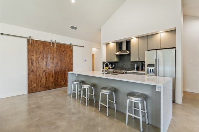 kitchen with wall chimney range hood, a kitchen island with sink, tasteful backsplash, and a kitchen breakfast bar