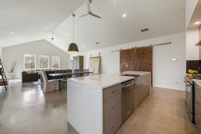 kitchen with a barn door, a center island with sink, ceiling fan, and appliances with stainless steel finishes