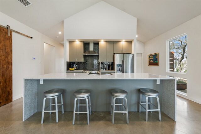 kitchen with a barn door, high quality fridge, wall chimney range hood, gray cabinets, and a breakfast bar area