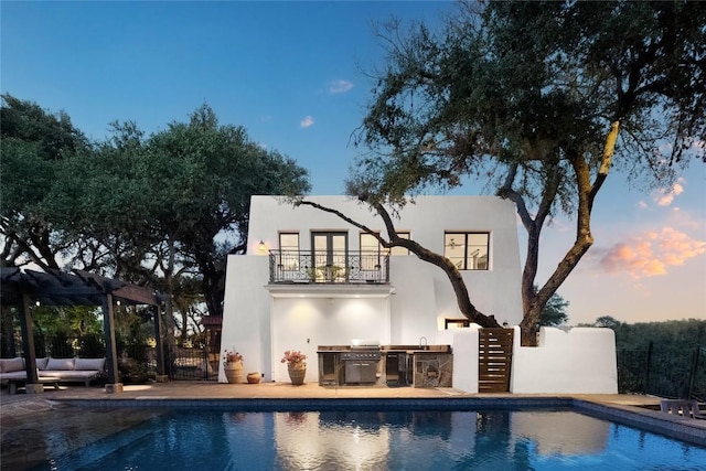 429 Sunfish St, Lakeway, TX 78734 - back of house at dusk featuring an outdoor kitchen, a balcony, an outdoor pool, stucco siding, and a patio area