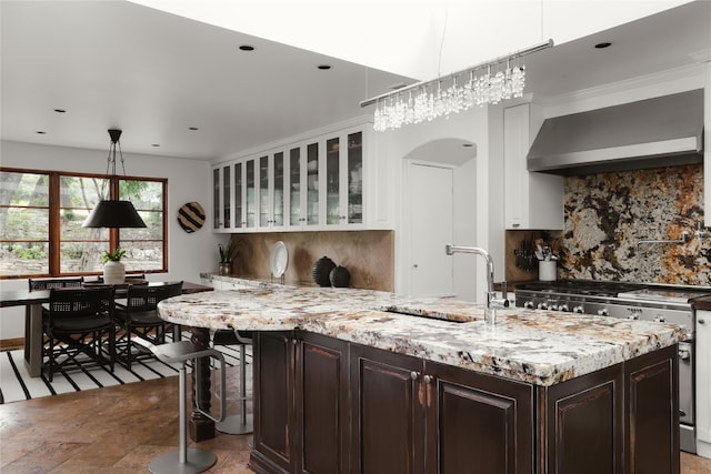 kitchen featuring hanging light fixtures, high end stainless steel range oven, wall chimney exhaust hood, tasteful backsplash, and dark brown cabinetry