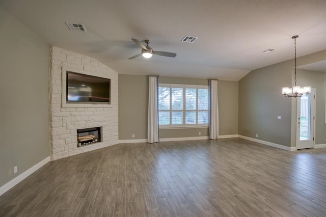 unfurnished living room with dark hardwood / wood-style floors, ceiling fan with notable chandelier, a stone fireplace, and lofted ceiling