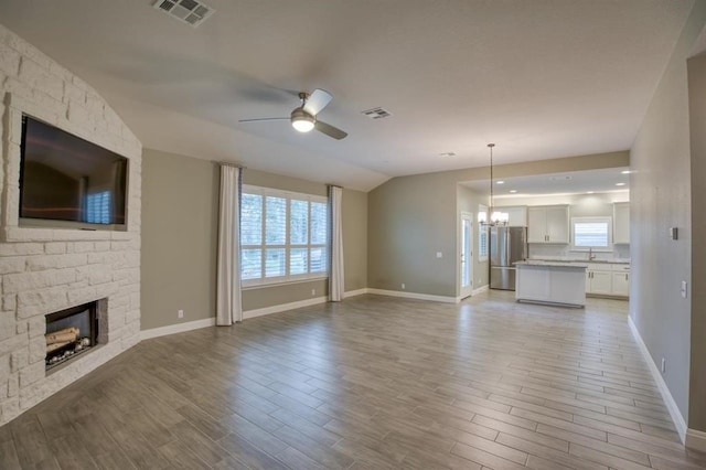 unfurnished living room featuring a stone fireplace, light hardwood / wood-style floors, plenty of natural light, and ceiling fan with notable chandelier