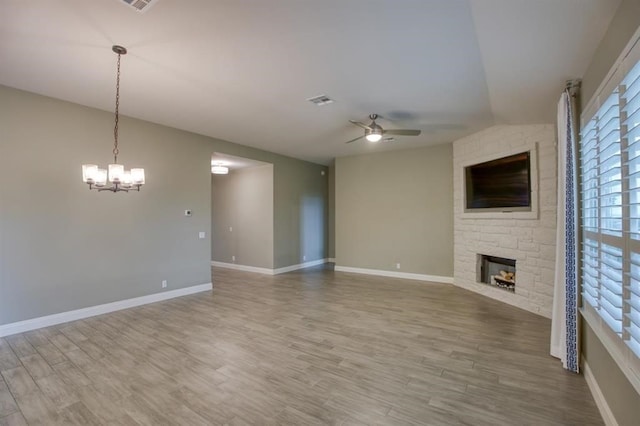 unfurnished living room featuring brick wall, ceiling fan with notable chandelier, a fireplace, and wood-type flooring