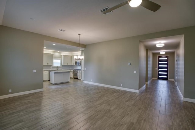 unfurnished living room with dark hardwood / wood-style flooring, sink, and ceiling fan with notable chandelier