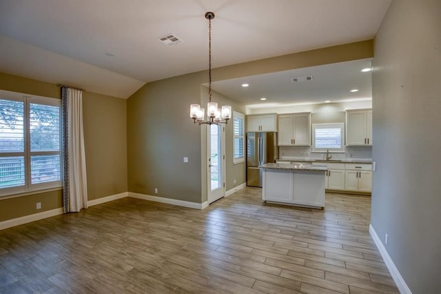 kitchen featuring a kitchen island, stainless steel fridge, decorative light fixtures, white cabinetry, and a chandelier