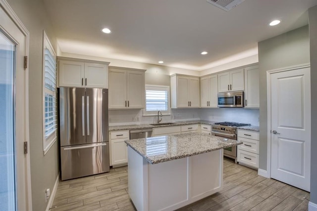 kitchen featuring white cabinets, a kitchen island, stainless steel appliances, light stone countertops, and sink