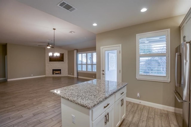 kitchen featuring light hardwood / wood-style floors, a center island, a fireplace, white cabinetry, and stainless steel refrigerator