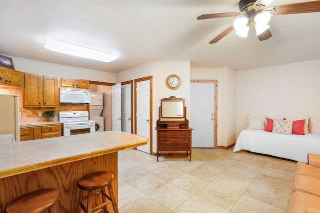 kitchen featuring white appliances, backsplash, tile counters, a kitchen bar, and ceiling fan