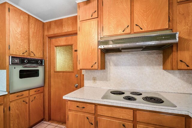 kitchen with electric cooktop, backsplash, ornamental molding, stainless steel oven, and light tile patterned flooring