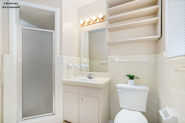 bathroom with a shower with door, vanity, toilet, and tile walls