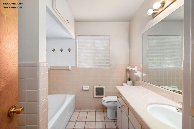 bathroom with toilet, tile patterned floors, vanity, a washtub, and tile walls