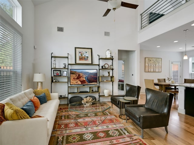 living room featuring ceiling fan, light hardwood / wood-style flooring, a high ceiling, and plenty of natural light