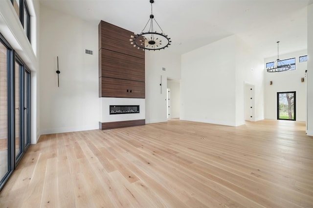 unfurnished living room featuring an inviting chandelier, light hardwood / wood-style floors, and a towering ceiling