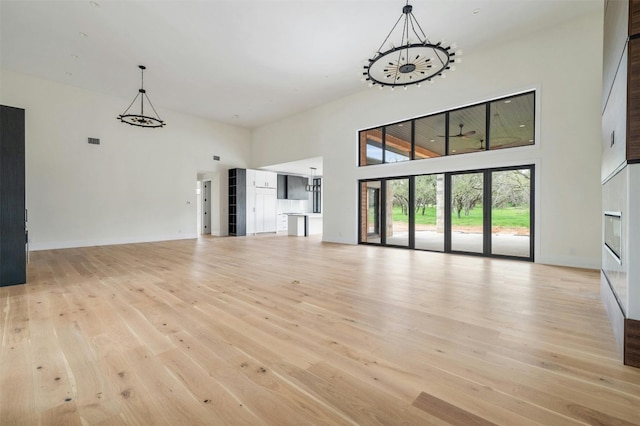 unfurnished living room featuring a notable chandelier, light hardwood / wood-style floors, and a high ceiling