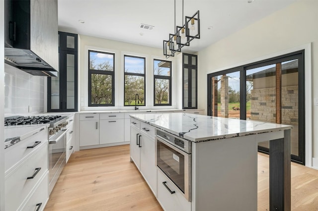 kitchen featuring a kitchen island, wall chimney range hood, tasteful backsplash, appliances with stainless steel finishes, and hanging light fixtures