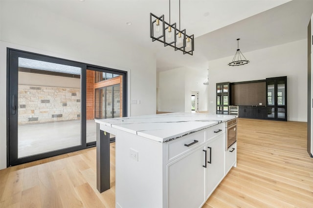 kitchen featuring decorative light fixtures, light hardwood / wood-style floors, white cabinets, a center island, and light stone countertops