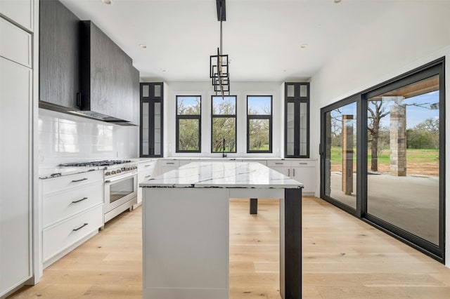 kitchen featuring pendant lighting, a kitchen island, light stone countertops, high end stove, and light wood-type flooring