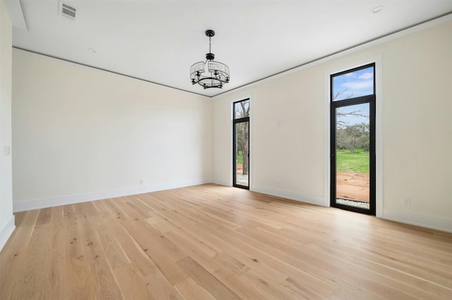 spare room with an inviting chandelier, a wealth of natural light, and light wood-type flooring